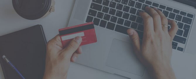 A person using a laptop holding a red credit card.