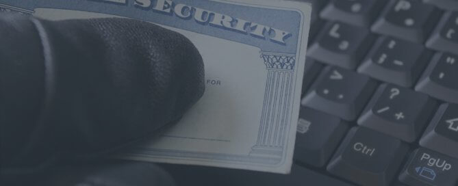 A hand wearing a black glove holding a social security card over a keyword.