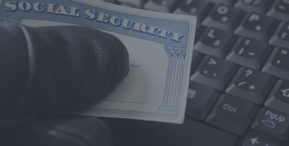 A hand wearing a black glove holding a social security card over a keyword