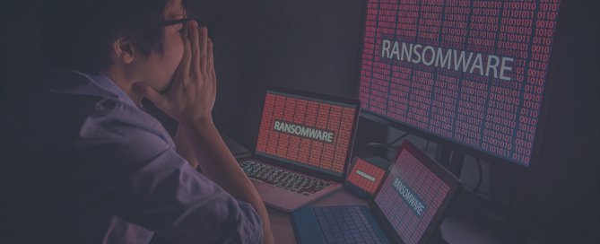 A Asian man with his hand over his face sees ransomware on his computer.