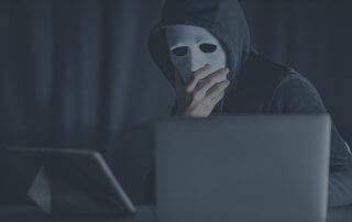 A person wearing white mask and dark hoodie using a computer.