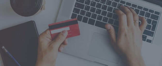 A laptop on a white table and a person holding a red credit card.