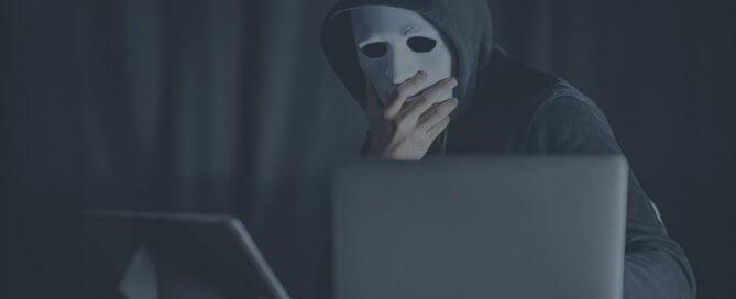 A person wearing white mask and dark hoodie using a computer.