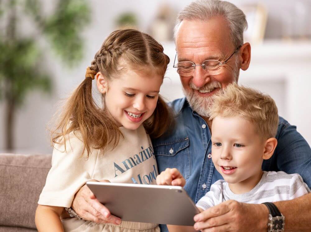 A grandparent with his grand kids holding a tablet.