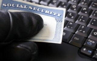 A hand is wearing a black glove holding a social security card over a keyboard.