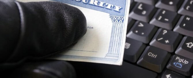 A hand is wearing a black glove holding a social security card over a keyboard.