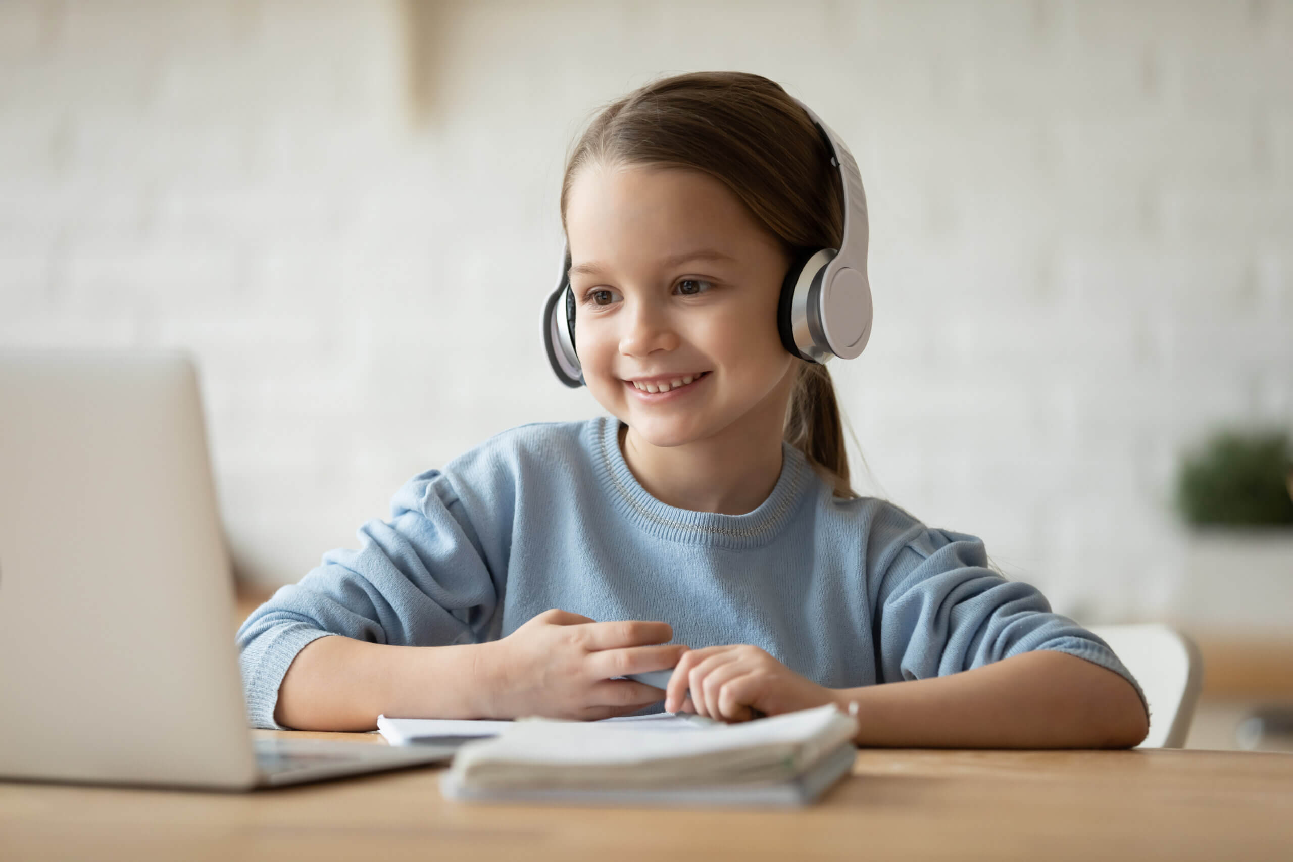 Little schoolgirl learning school subject distantly using pc and headphones.