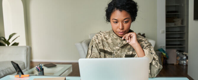 Multiracial soldier woman wearing military uniform looking at the laptop screen.