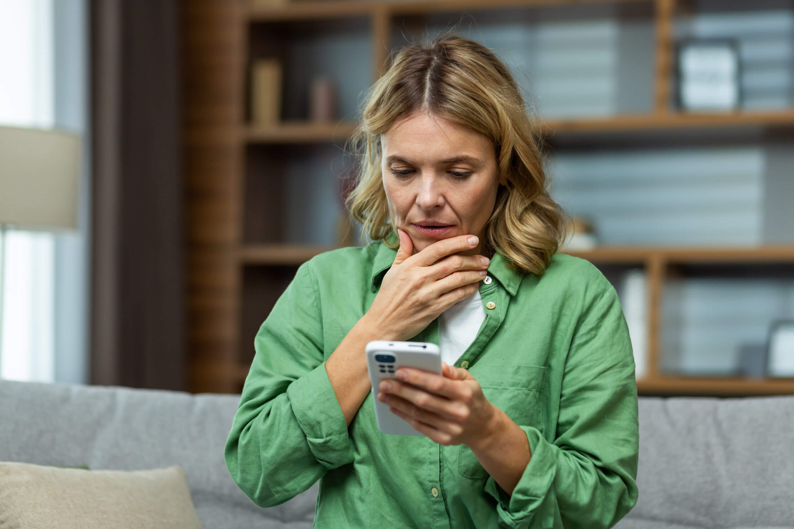 Worried woman sitting on sofa at home holding phone.